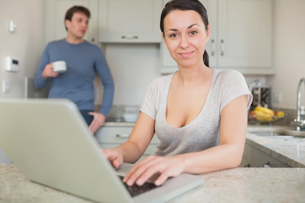 Young woman using laptop with man drinking coffee