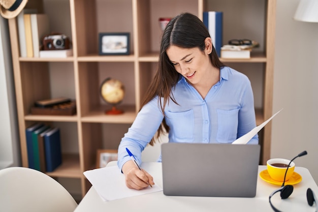 Young woman using laptop writing on document at home