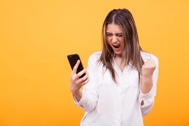 Young woman using mobile phone against yellow background