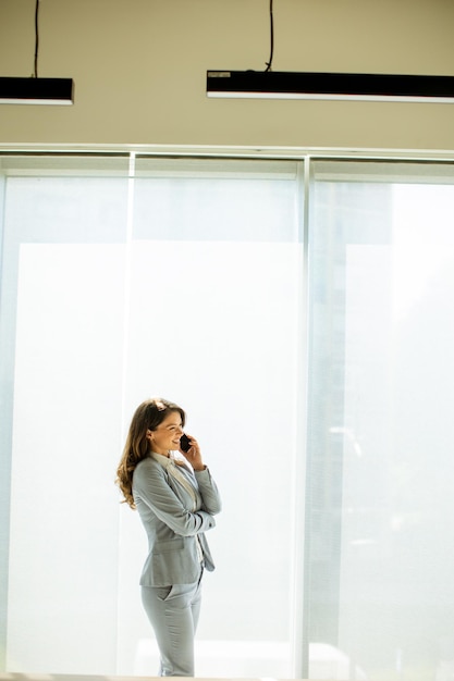 Young woman using mobile phone by the office window