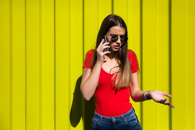 Young woman using mobile phone by the yellow wall