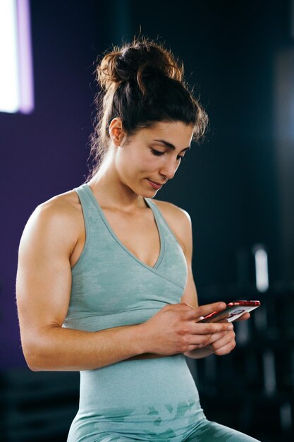 Foto giovane donna che usa il cellulare in palestra