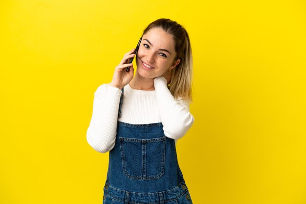 笑っている孤立した黄色の背景の上に携帯電話を使用して若い女性
