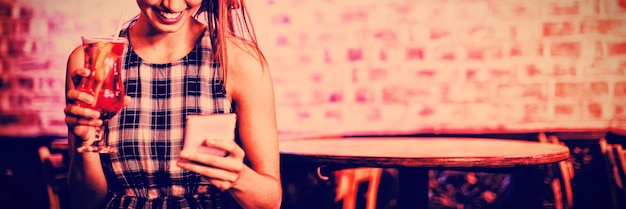 Young woman using mobile phone while having cocktail drink