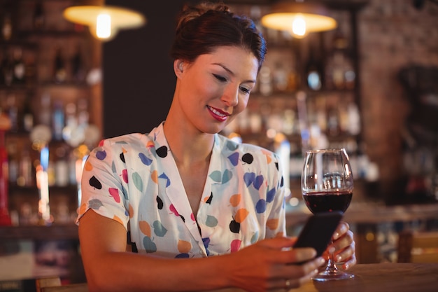 Young woman using mobile phone while having wine