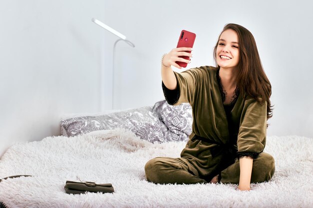 家のベッドに座っている間に携帯電話を使っている若い女性
