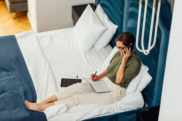 Photo young woman using mobile phone while sitting on bed