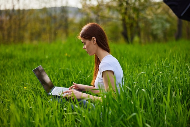 Фото Молодая женщина использует мобильный телефон, сидя на травянистом поле