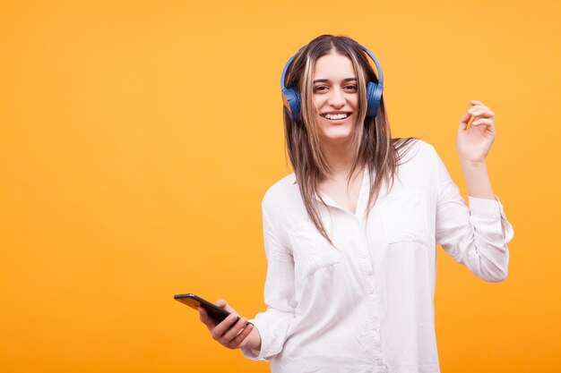 Young woman using mobile phone while standing against yellow background