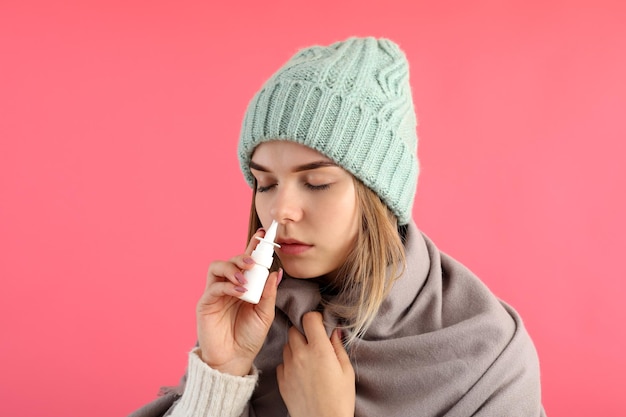 Young woman using nasal spray on pink background, runny nose concept