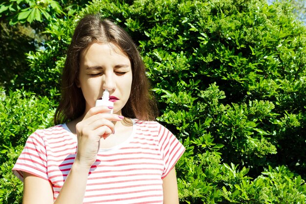 Young woman using nasal spray while standing against plants in park