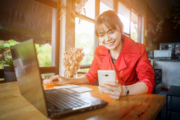 young woman using phone by laptop while sitting at home
