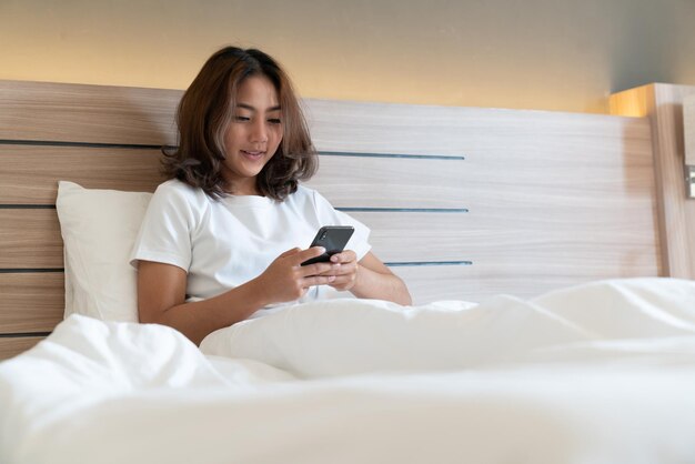 Young woman using phone while sitting on bed at home