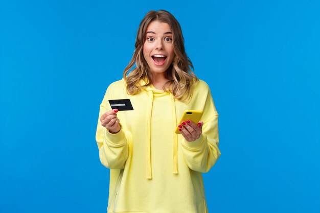 Young woman using phone while standing against blue sky