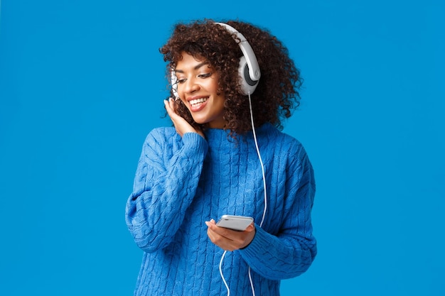 Young woman using phone while standing against blue sky