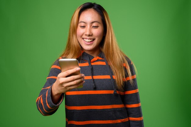 Young woman using phone while standing against green background