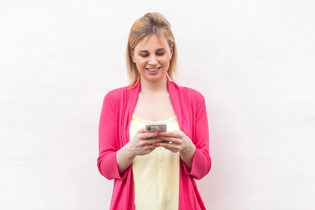 Young woman using phone while standing against wall