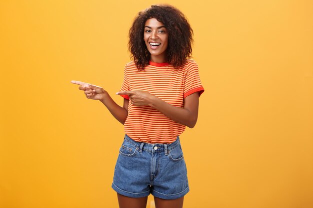 Young woman using phone while standing against yellow background