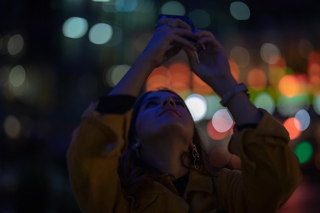 Photo young woman using phone while standing outdoors at night