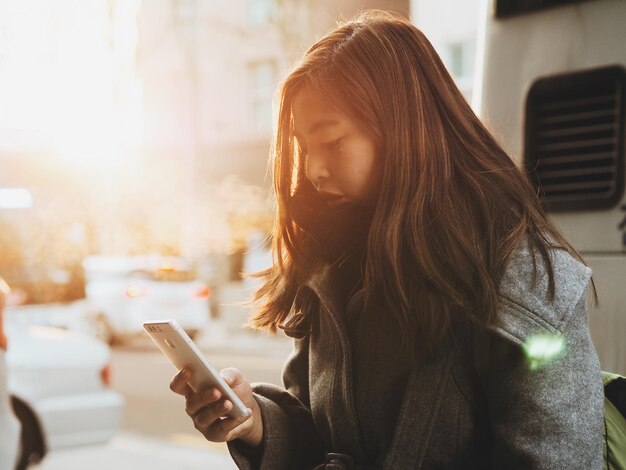 Young woman using phone while standing on road in city