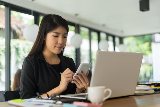 Young woman using phone with laptop on desk in office