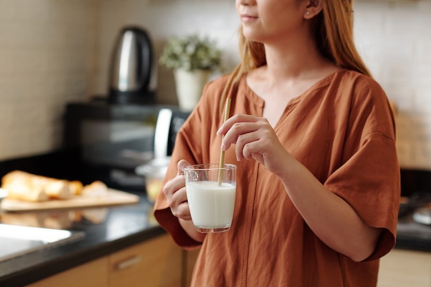 Young woman using reusable bamboo straw when drinking cup of milk