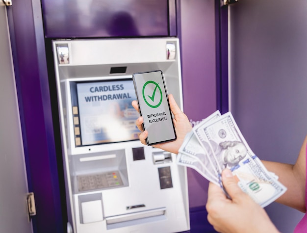 Photo young woman using the smart phone for cardless withdrawing the cash near the atm