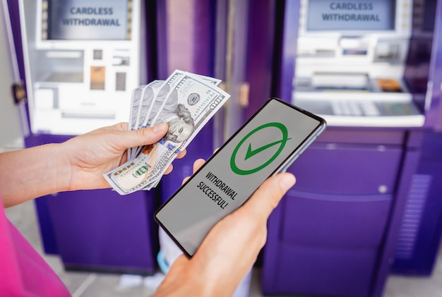 Photo young woman using the smart phone for cardless withdrawing the cash near the atm