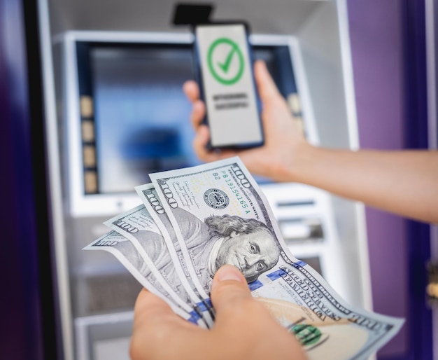 카드 없는 현금을 ATM 근처에서 인출하기 위해 스마트폰을 사용하는 젊은 여성