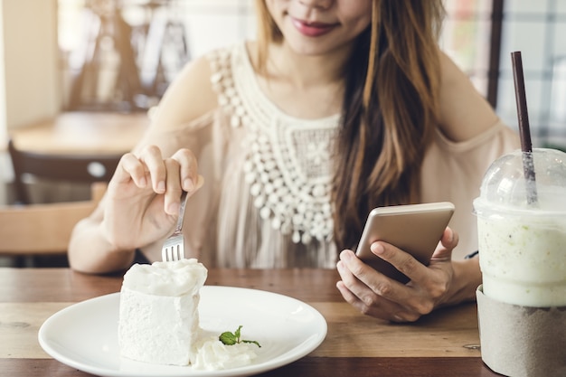 Giovane donna utilizzando smart phone e mangiare la torta nella caffetteria