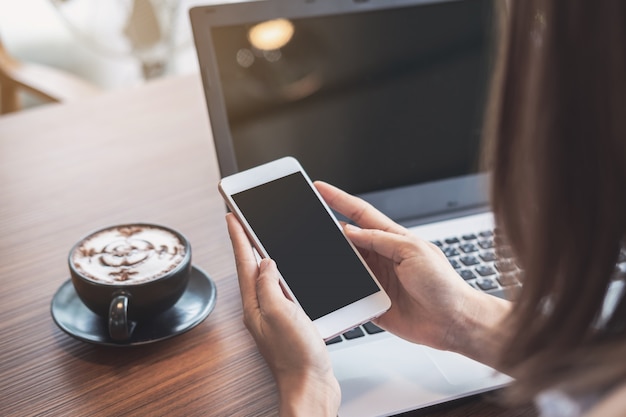 Young woman using smart phone and laptop with cup of coffee in cafe