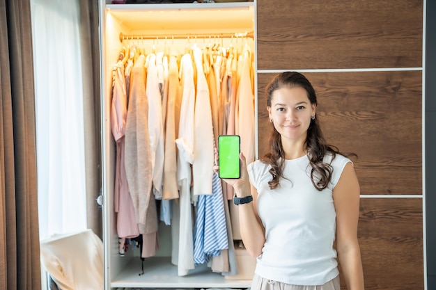 Foto giovane donna che utilizza un'app per smartphone per la vendita di vecchi vestiti indesiderati nell'app chroma green screen