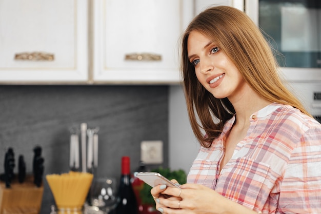 Young woman using smartphone in kitchen close up