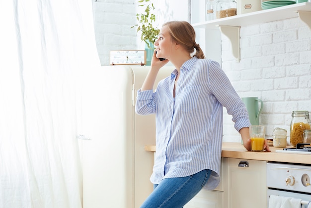 Young woman using smartphone leaning at kitchen table with coffee mug and organizer in a modern home. 