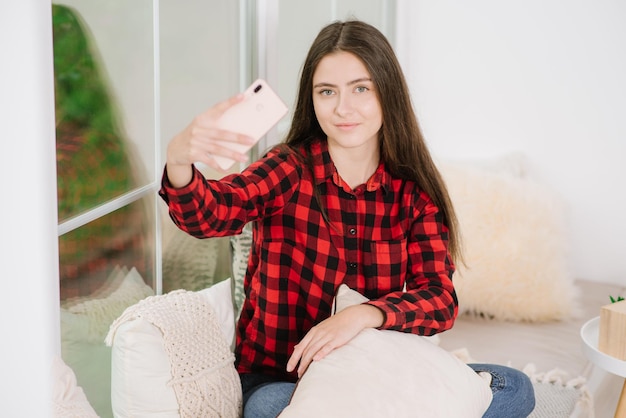 Photo young woman using smartphone near big window at home during quarantine