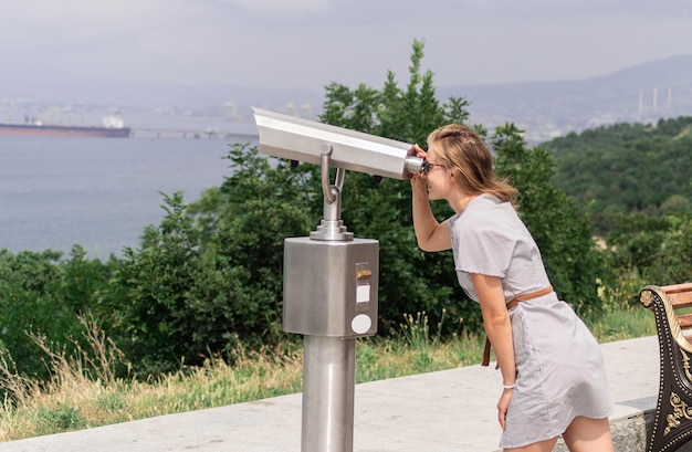 Photo young woman using stationary binoculars on a warm summer day on a hill against the background