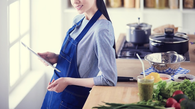 彼女の台所で料理するためにタブレットコンピュータを使用している若い女性