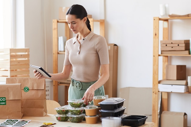 Young woman using tablet pc and checking the food while working in food delivery service