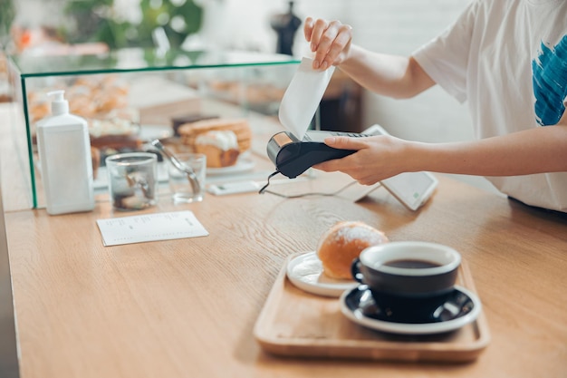 Young woman using terminal for contactless payment in coffee shop