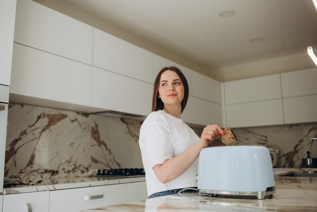 Young woman using toaster at table in kitchen