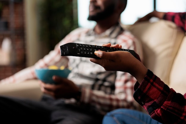 Young woman using tv remote control to switch channel program and find movie on television to watch. Eating takeaway delivery from fast food and watching film together. Close up.