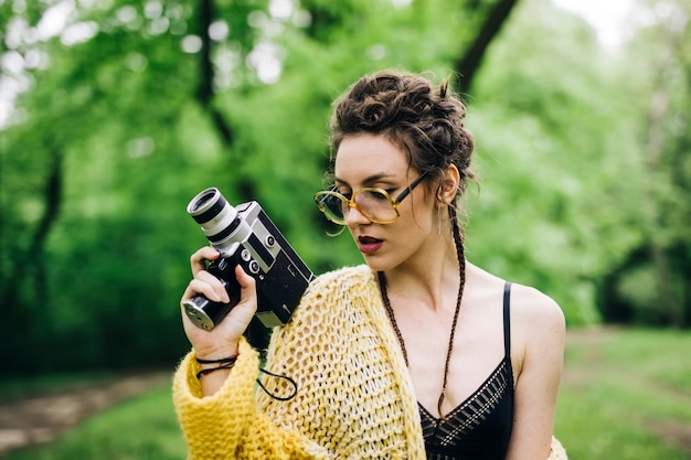 Foto giovane donna che utilizza una macchina fotografica del cinema dell'annata in un parco