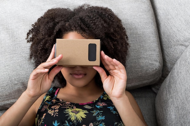 Photo young woman using virtual reality device cardboard vr on sofa