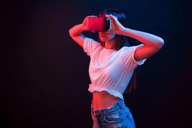 Giovane donna che utilizza occhiali per realtà virtuale in camera oscura con illuminazione al neon