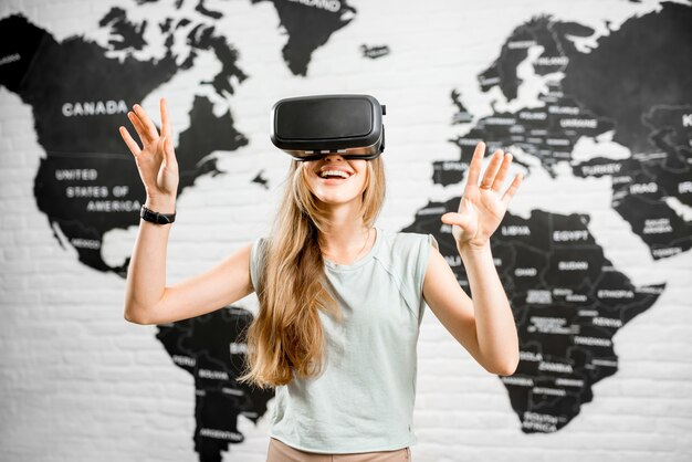 Молодая женщина в очках виртуальной реальности, сидя в помещении с картой мира на заднем плане