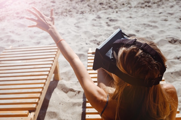 Foto giovane donna che usa un simulatore di realtà virtuale mentre è seduta su una poltrona in spiaggia