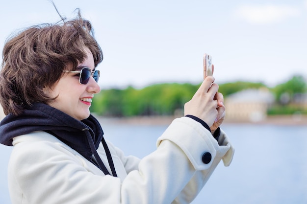 休暇中に携帯電話を使って川や街の写真を撮る若い女性