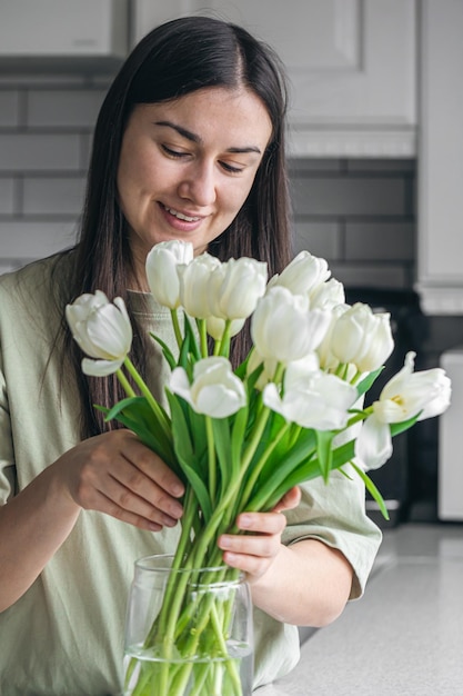 若い女性とキッチンの白いチューリップの花束の花瓶