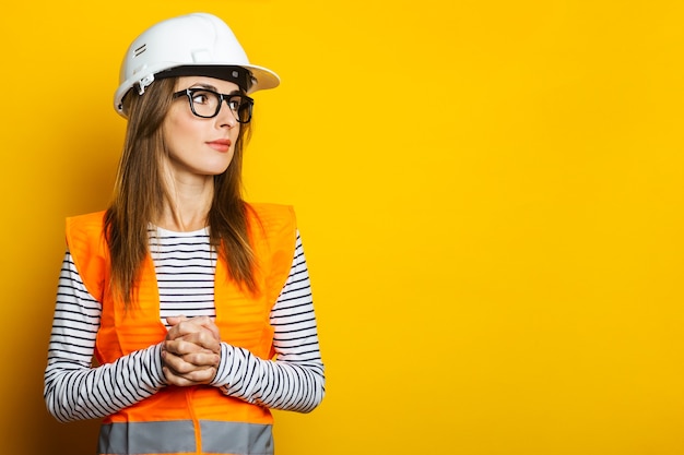 Young woman in a vest and hard hat on yellow