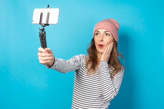 Young woman video blogger takes pictures of herself on the phone while broadcasting on a blue surface